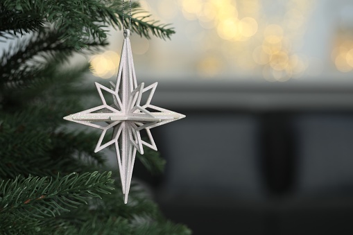 Closeup of beautiful bauble in shape of star hanging on Christmas tree. Space for text