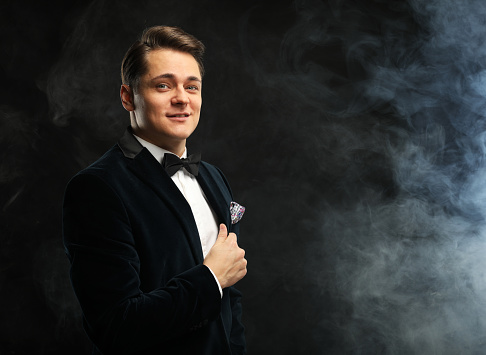 Stylish young man in a tuxedo holding a microphone, posing against a dark background with smoke