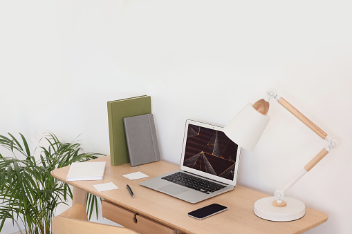 Cozy workspace with laptop, smartphone and lamp on wooden desk at home