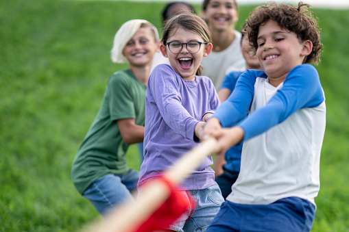 A small group of school aged children pull a rope with all their might, as they participate in a game of tug-of-war.  They are each dressed casually and are smiling and laughing as they pull together.