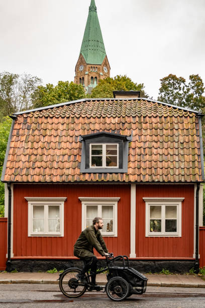 Stockholm, Sweden Oct 2, 2023 A man on a cargo bike passes a  classic red Swedish house on Malmgardsvagen on Sodermalm.