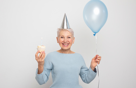 People, party, aging and maturity concept. Beauitful elderly female wearing conical hat celebrating birthday