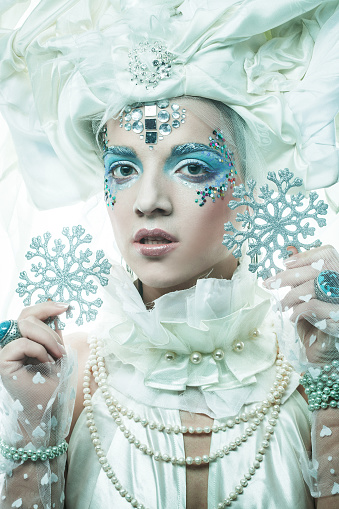 Party, christmas and people concept: Young beautiful woman with creative make-up in a New Year's style holds a silver snowflakes near her face. Snow queen, fairy.