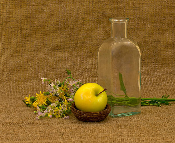 Empty bottle, apple and flowers on background of burlap