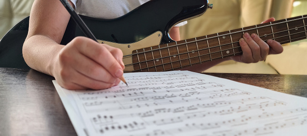 Composer child girl hand writing notes in notebook closeup. Musician composing music while sitting with guitar and child learning