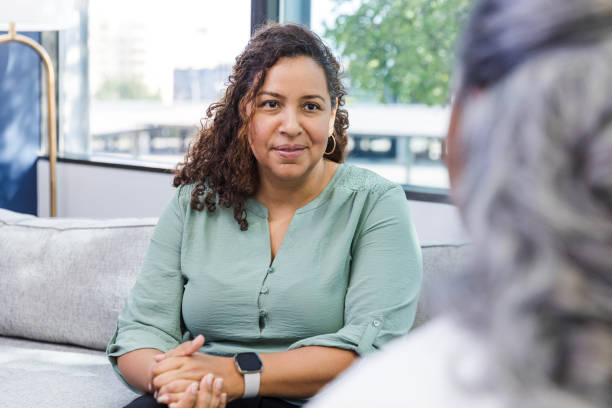 Mature woman focuses on unrecognizable senior female friend The mature adult woman clasps her hands and listens attentively to her unrecognizable senior adult female friend. melancholy computer support specialist stock pictures, royalty-free photos & images