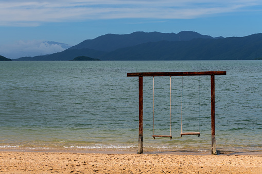 View of woman swinging on white sand beach relaxing and sunbathing by the lagoon in Mexico