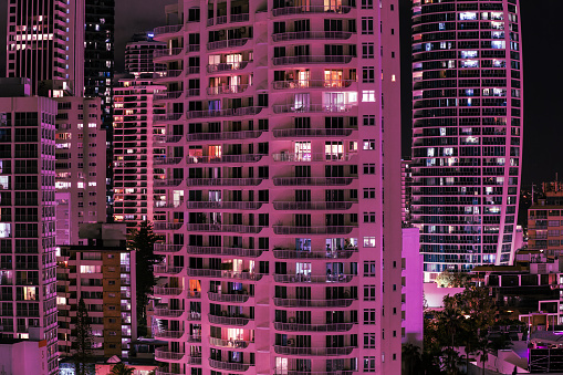 Building facades at night with patterns created by lights,and  dark through windows in pink hue..