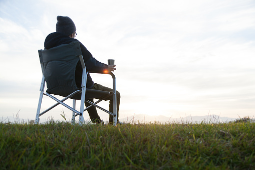 a man is sitting in a chair, sipping coffee while watching the sunrise