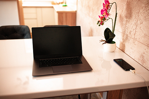 Laptop and phone charging on wooden table in dinning room