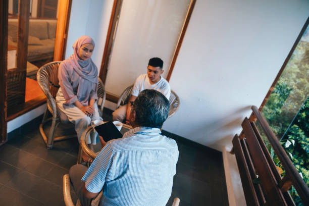 Three people are talking in the office. The psychologist is talking to the patient. Therapist gestures. A woman psychotherapist conducts a consultation of a married couple husband and wife. Solving interpersonal conflicts, co-dependent or abusive relationships in the family. Coach advice on personal or financial matters, Real estate agent, insurance agent, home purchase, pregnancy planning, reproductive specialist