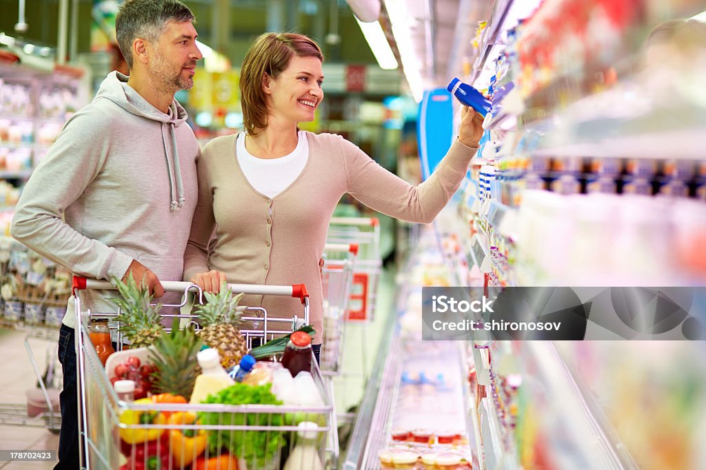 A mature couple choosing products in a supermarket Image of happy couple with cart choosing products in supermarket Supermarket Stock Photo