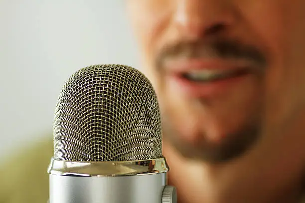 A close-up shot of a microphone with an announcer in the background recording a voice over.