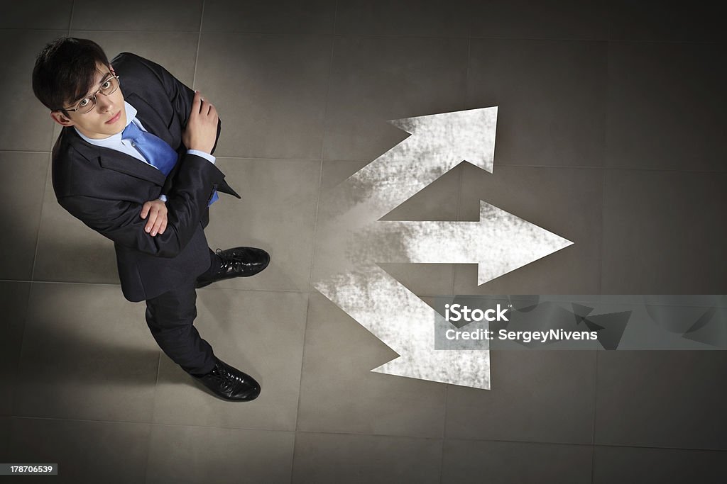 Man wearing a suit with arms folded and white arrows Top view of businessman standing against directions background Abstract Stock Photo