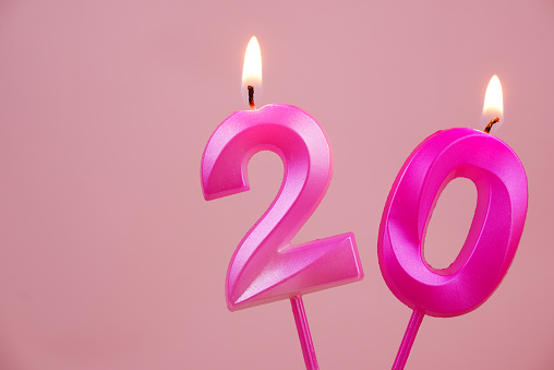 Pink birthday candles with burning on pink background. Number 20. Copy space for text.