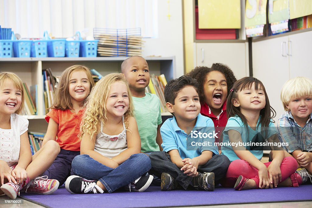 Group of Elementary Pupils In Classroom Group of Elementary Pupils In Classroom Looking Away From Camera Laughing Whilst Sitting Down Classroom Stock Photo