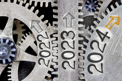 Photo of tooth wheel mechanism with numbers 2024, 2023, 2022 and arrows imprinted on metal surface. New Year concept.