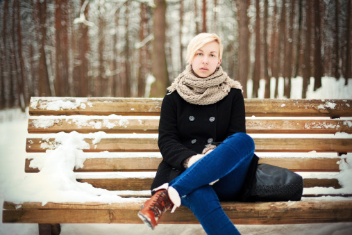Young blonde woman sitting on a bench in winter park