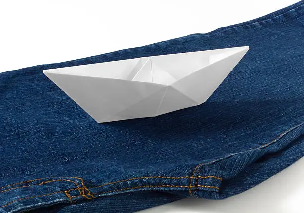 A paper boat sailing on a blue stream made of a pair of blue jeans