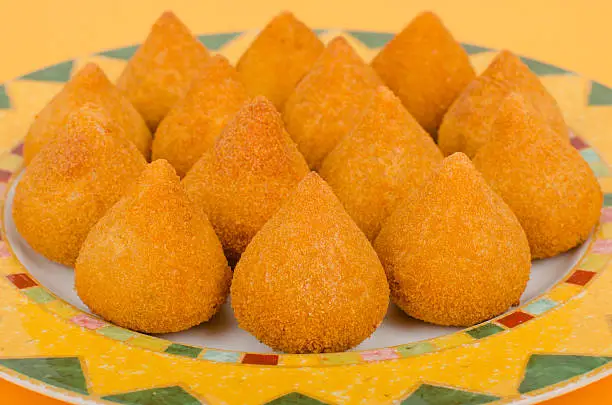 Coxinha de Galinha - Brazilian breaded and deep fried snacks filled with shredded chicken on a colourful plate on a orange background.