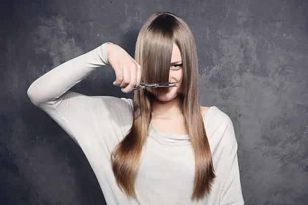 Photo of Young woman with scissors trimming her bangs