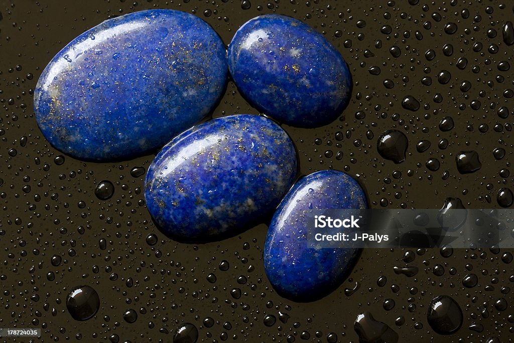 Lapis lazuli gems on the black background. Beautiful closeup picture of polished lapis lazuli gemstones in the wet black background. Lapis Lazuli Stock Photo