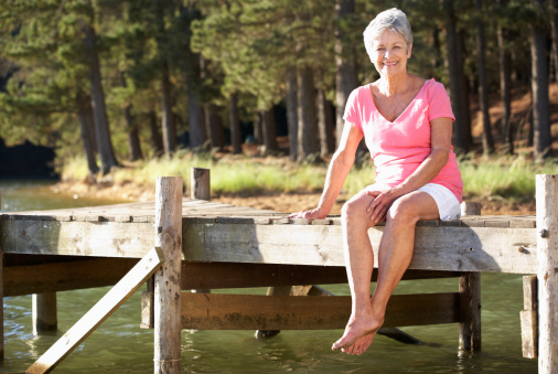 Senior woman sitting by lake smiling to camera