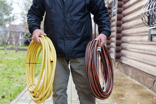 Garden hoses in the hands of a man in the garden near a wooden house. High quality photo