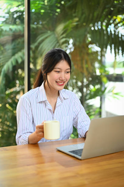 istock Happy Asian female office worker drinking coffee and working on laptop computer 1787282092