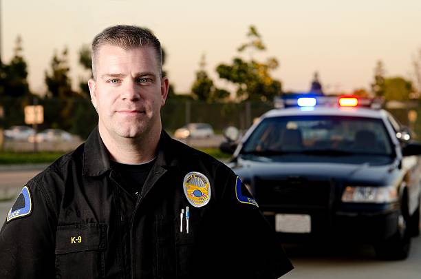 Patrol officer A K9 police officer wearing a BDU uniform standing in front of his patrol car. police dog handler stock pictures, royalty-free photos & images