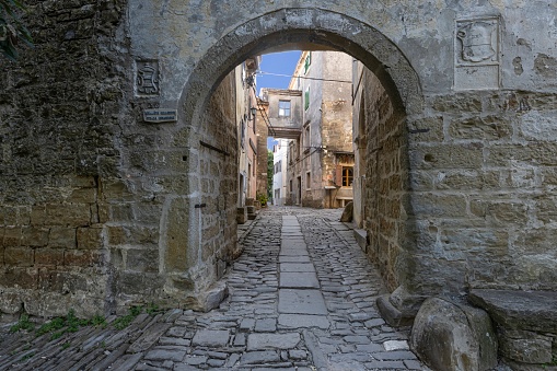 View through an arched gateway along a cobbled street into an ancient village without people during the day