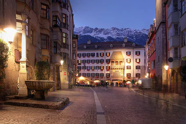 The Golden Roof as seen from along the pedestrian Herzog-Friedrich Street in evening in Innsbruck, Austria. Some fresh snow is covering the peaks of the Alps hoovering over the city.