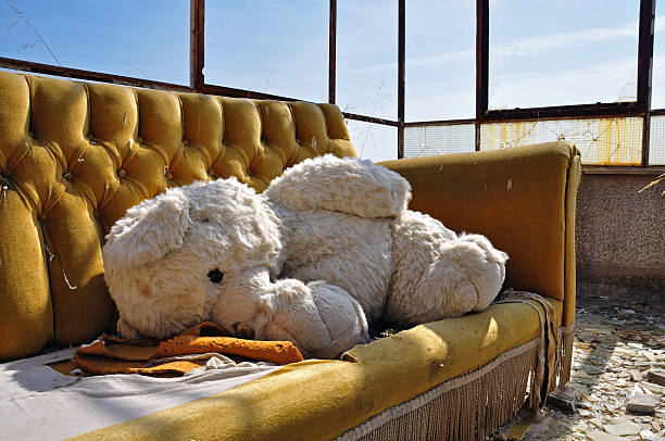 Vintage teddy bear and couch in abandoned building. Social issues.