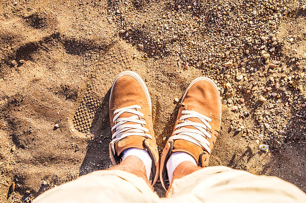 Pair of Boots Shoes man's Foot on a sand sea-side beach view from above Summer Leisure time background