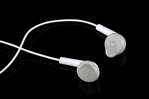 Wired white earbuds isolated on a black reflective surface