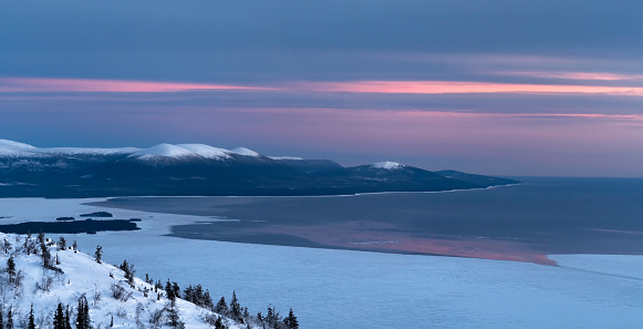 Stunning winter panoramic landscape. Amazing nature of the North. Purple sunset stripes on the sky. Winter twilight. Winter postcard view of the night mountains and White Sea under the snow.