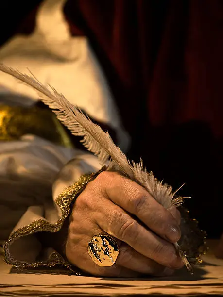 A senior man's hand holding a quill and wearing a signet ring with seal