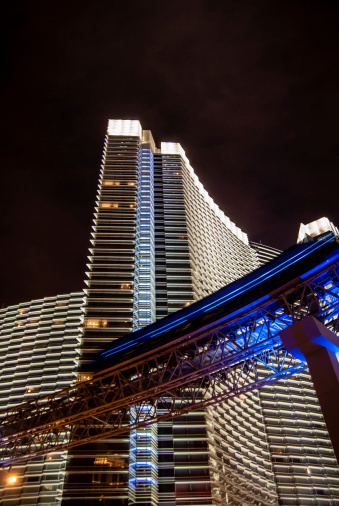 The streaking blue blur of a speeding night tram passes beneath a soaring, modern skysvraper.