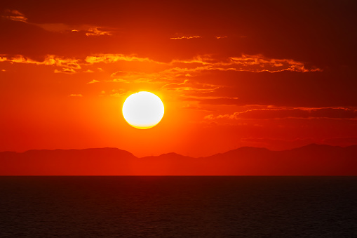 The sun setting over mountains on the horizon at sea.
