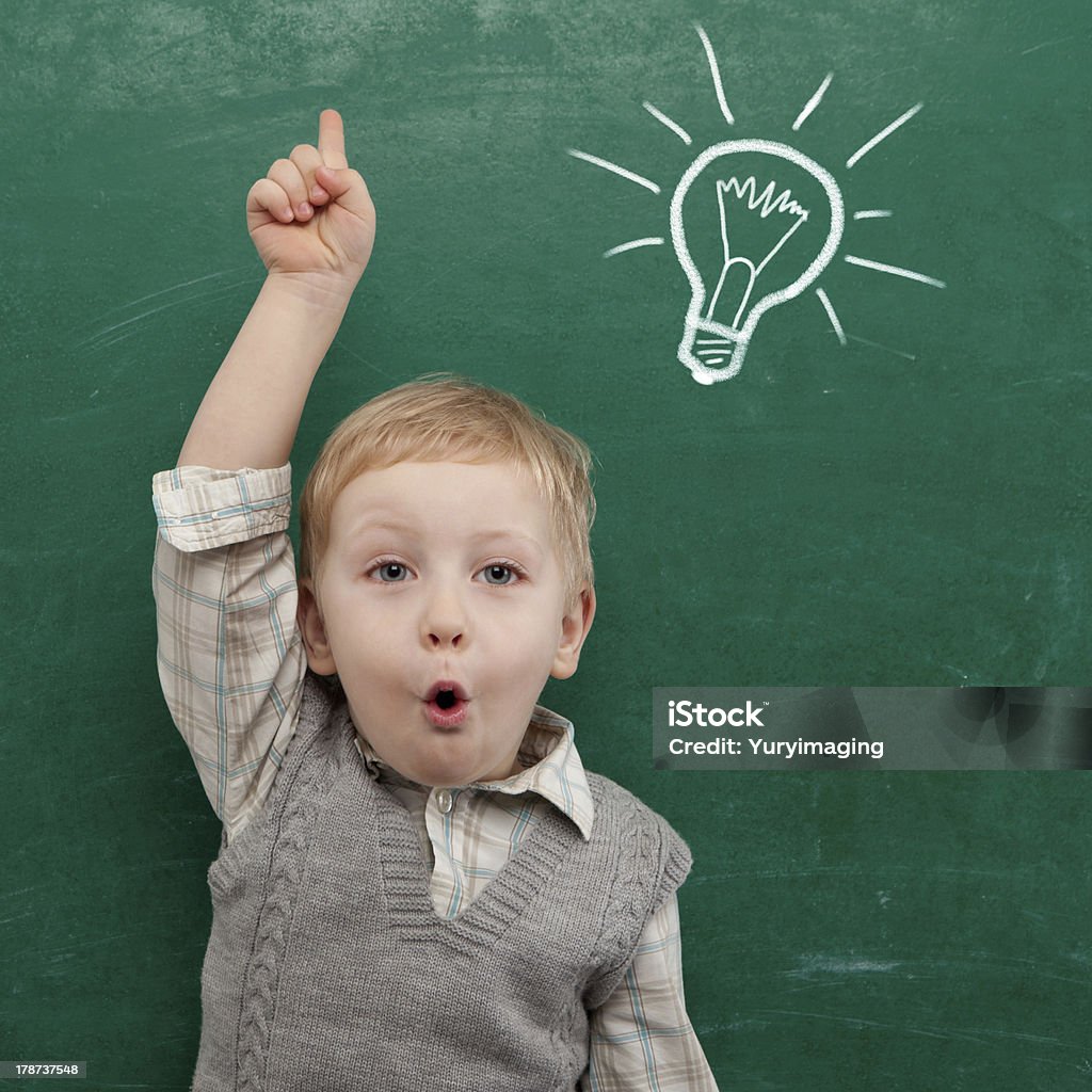 Young child under light bulb drawn on chalkboard Cheerful smiling child at the blackboard. School concept Beautiful People Stock Photo