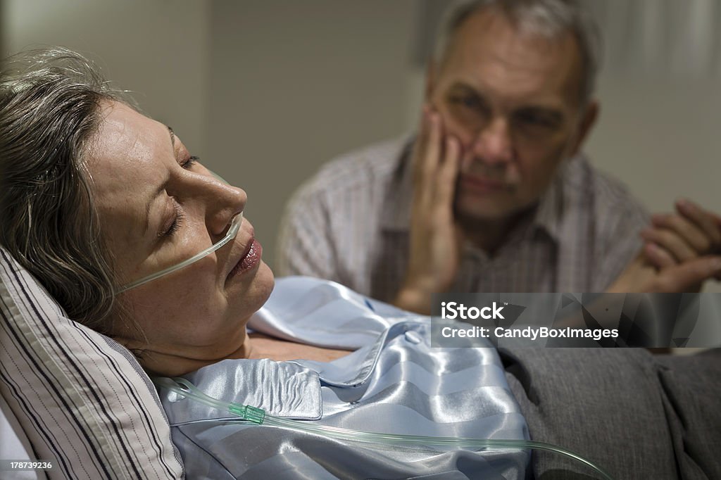 Sick mature woman lying in bed Sick mature woman lying in bed worried husband holding hands Illness Stock Photo