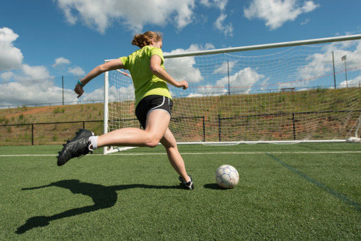 Young adult female soccer player practices shots on goal on a beautiful turf field