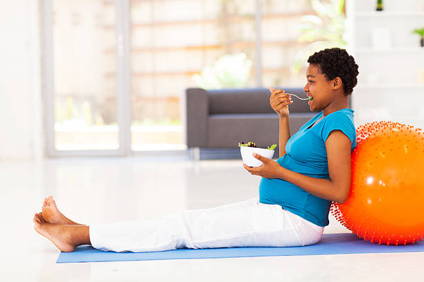 妊娠アフリカ系アメリカ人の女性に食べる、ヘルシーなサラダ、エクササイズマット - human pregnancy prenatal care relaxation exercise ball ストックフォトと画像