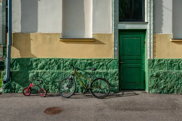 Two bicycles parked near the walls of a house with a green door. Saldus train station, Latvia.