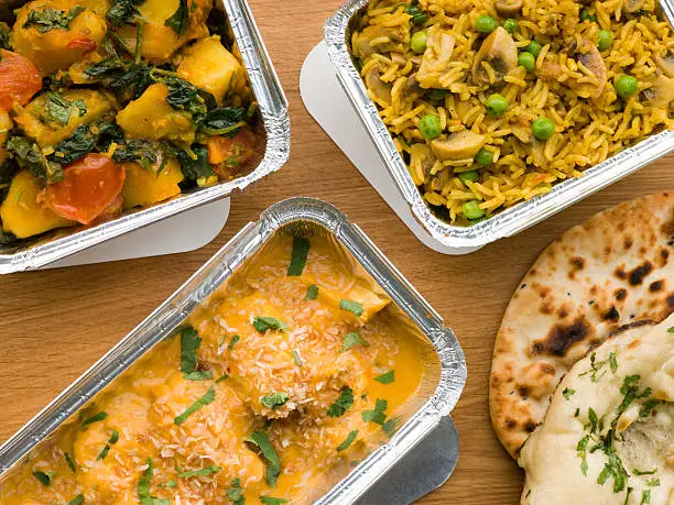 Above View Of Selection Indian Take Away Dishes In Foil Containers On Wooden Table