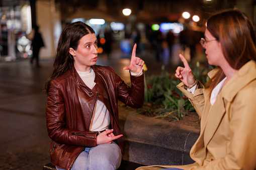 Delve into a nighttime sign language connection as two friends embrace communication on a silent street bench