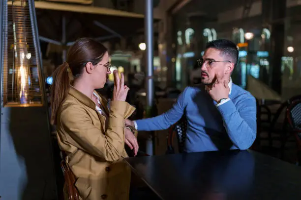 Photo of Couple Communicates through Sign Language in a Cozy Cafe Garden under Moonlit Sky