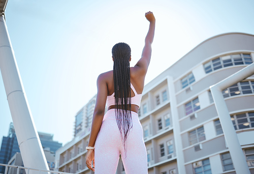 Strong, empowerment and black woman for fitness, exercise and workout outside in city showing fist, motivation and power. African athlete female showing support against urban building in South Africa