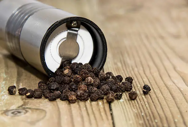 Peppershaker with Peppercorns on wooden background