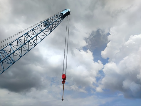 Selective focus on hook hanging on crane boom against bright blue and cloudy sky background